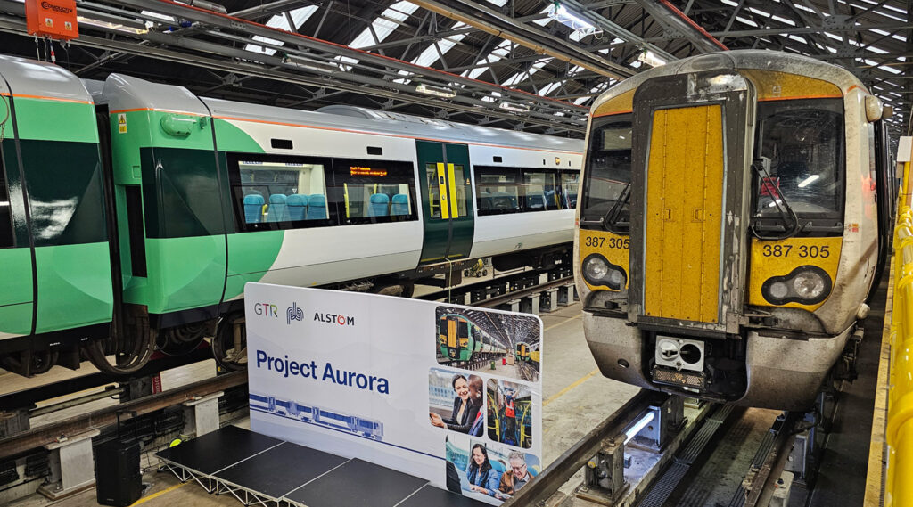 Deux trains dans un dépôt avec un panneau pour le "Projet Aurora" visible entre eux.