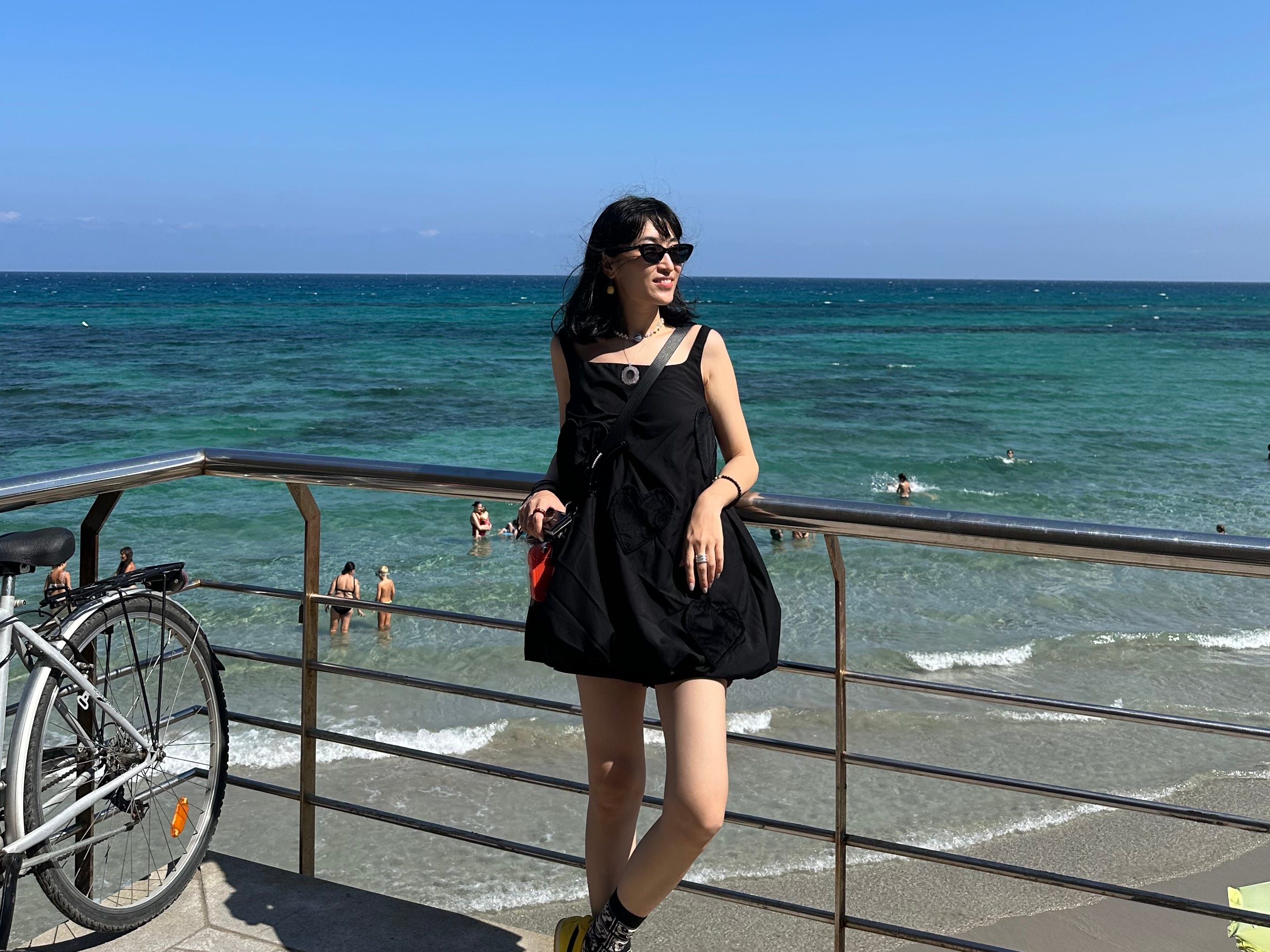 Une femme en robe noire posant près de la mer en Italie.