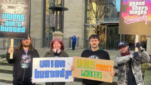 Des employés manifestent contre les licenciements à l'extérieur d'un bâtiment
